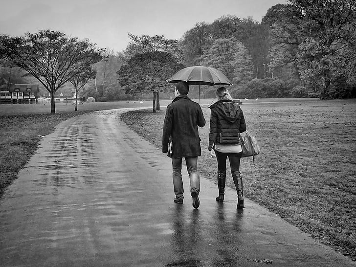 grayscale photo of couple walking on pavement while raining