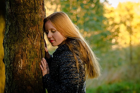 selective focus photography of woman in black top leaning on tree trunk