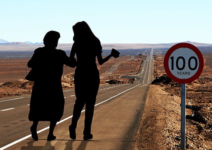 silhouette photo of two women walking down the street with 100 years signage