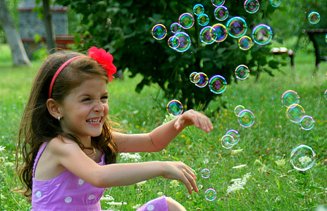 girl wearing pink dress sitting on grass near bubbles