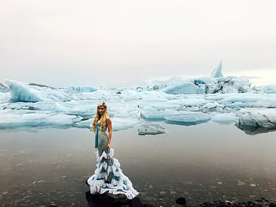 woman wearing white and green dress standing beside sea covered with ice blocks