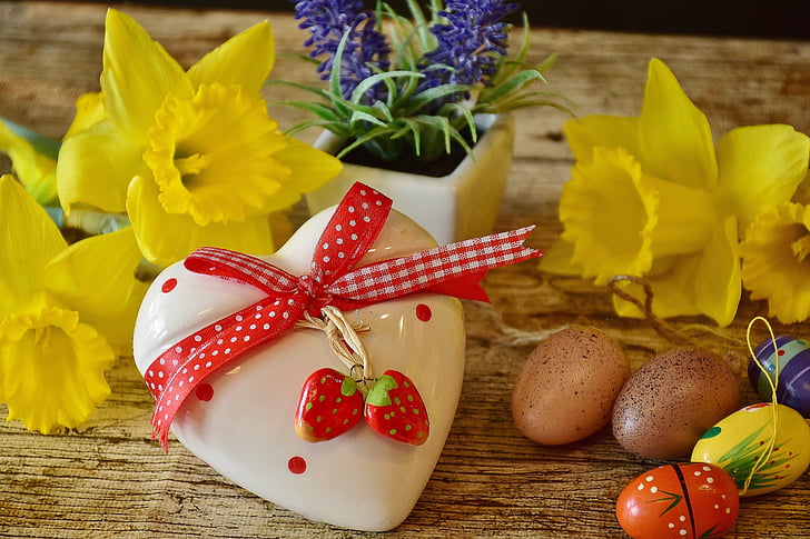 white and red ceramic heart lid near two yellow flowers on brown wooden surface
