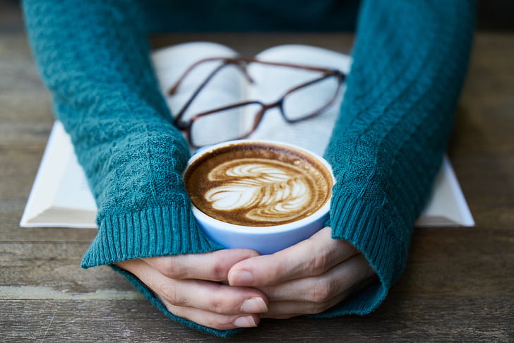 person's hand holding white ceramic coffee mug filled with latte
