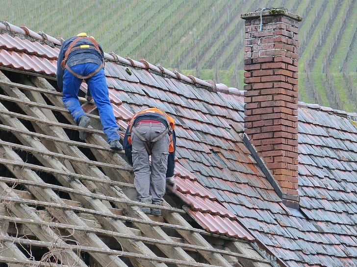 two person putting roof tiles on roof at daytime
