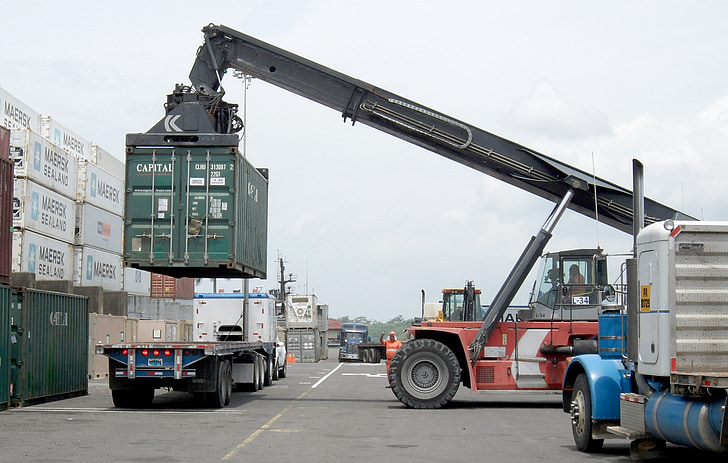 red and black heavy equipment carrying green intermodal container