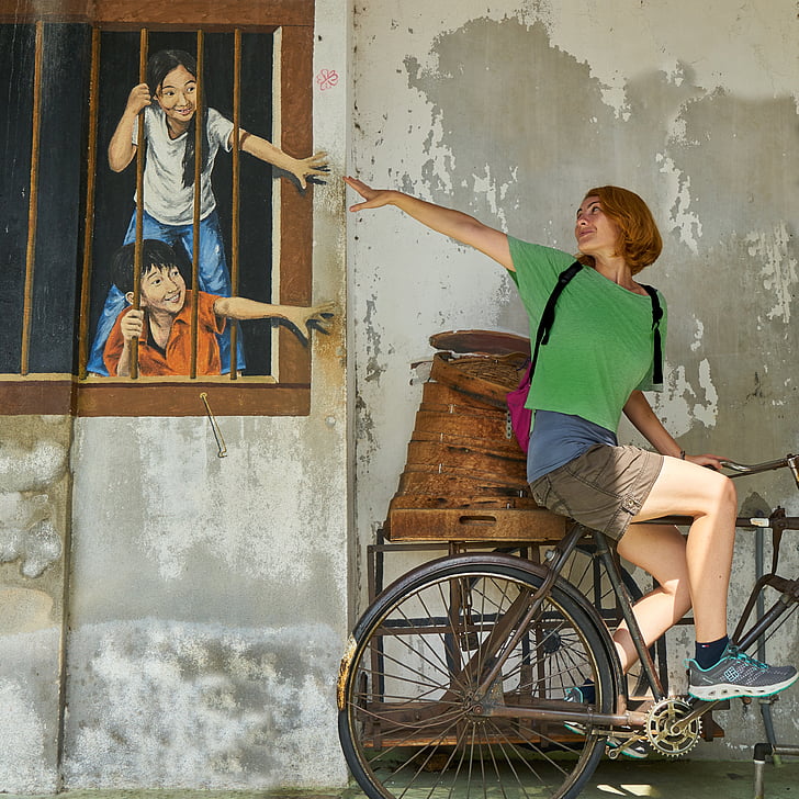 woman wearing green riding bicycle near wall art