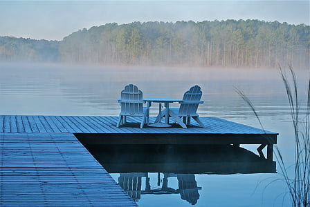 two white wooden adirondack chairs on wooden dock near lake