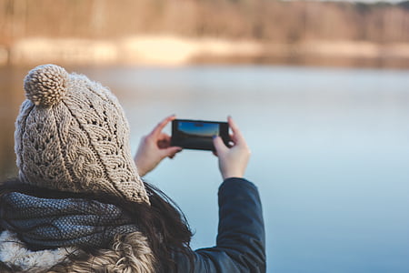woman in black leather jacket holding smartphone taking picture of body of water
