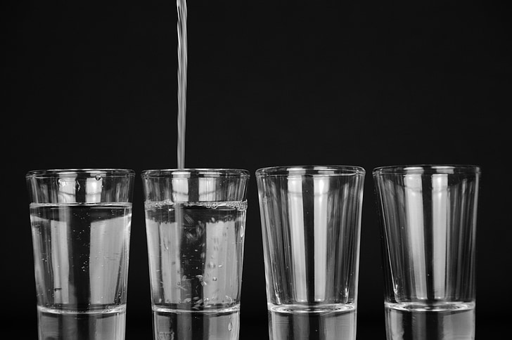 grayscale photo of two water-filled drinking glasses and two empty glasses