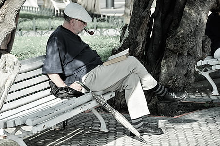 man in black shirt sitting on bench reading book