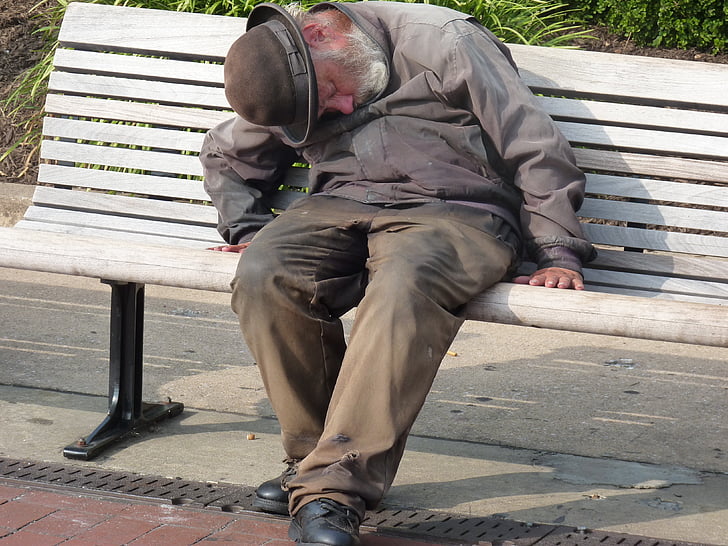 man in gray dress shirt and pants sleeping in gray wooden bench during daytime