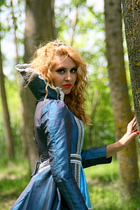 woman wearing blue medieval dress near tree trunks