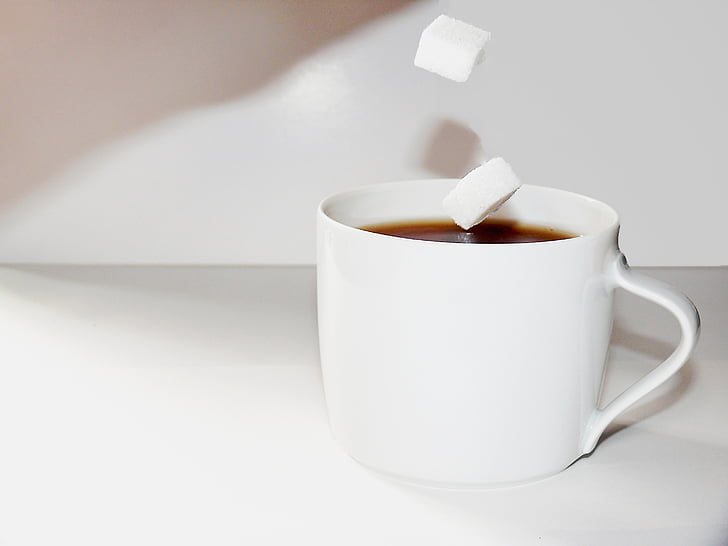 white ceramic teacup filled with black liquid and sugar cube