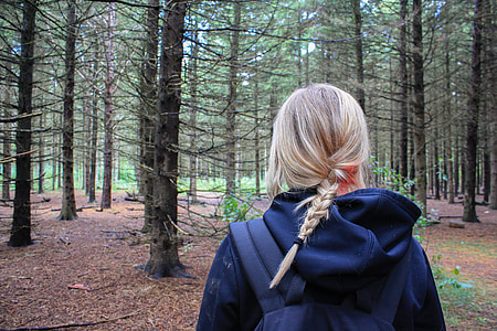 girl wearing blue hoodie standing near trees in the middle of the forest