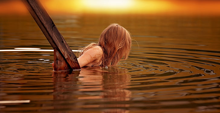blonde haired woman on water near wood