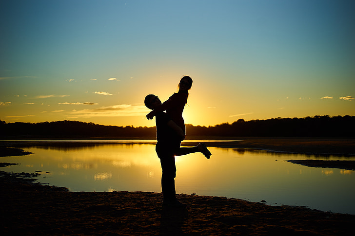silhouette photography of man carrying woman near lake