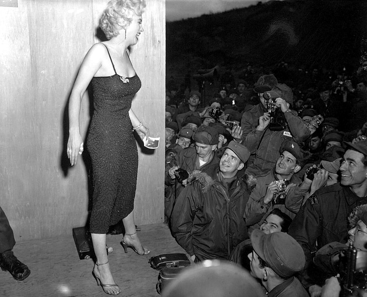 grayscale photo of Marilyn Monroe standing on stage in front of crowd