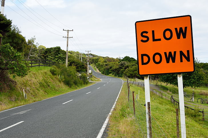 photo of asphalt road beside slow down signboard