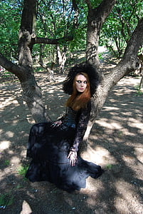 woman wearing black floral long-sleeved gown sitting on tree