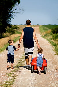 man walking with two children on brown road