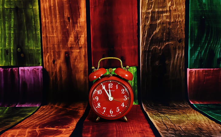 red analog alarm clock on brown wooden surface