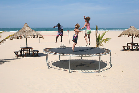 three children playing on round black trampoline near beach at daytime