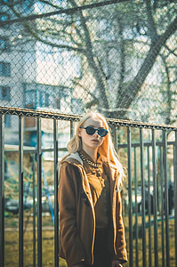woman wearing brown zip-up jacket and sunglasses near metal framed fence during daytime