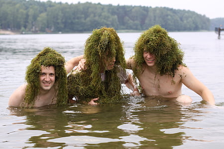 three person in body of water with green grasses on heads