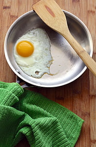 fried egg in round gray frying pan under brown wooden ladle