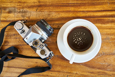 white ceramic teacup filled with coffee near gray DSLR camera