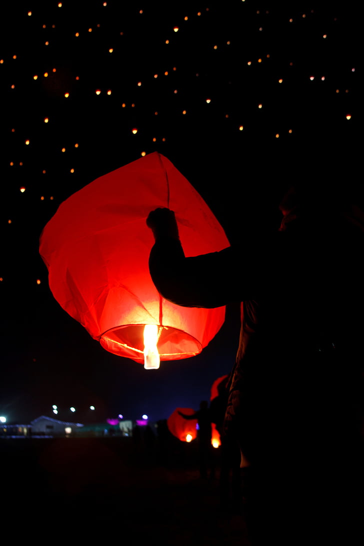man holding lighted sky lantern at night time