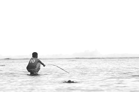 grayscale photo of man wearing shirt near body of water