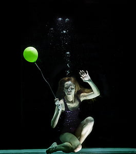 underwater photography of woman holding yellow balloon