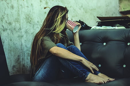 woman in blue jeans while drinking in a cup