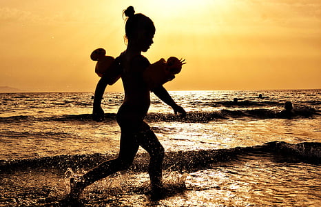 girl walking beside ocean during sunset