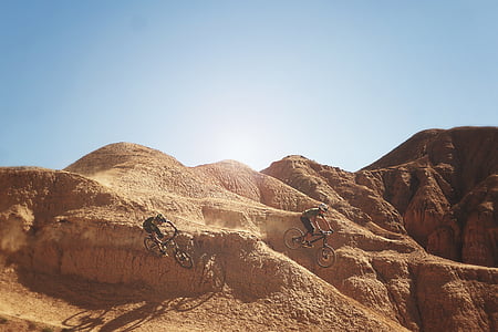 two man riding bicycle passing through brown land formations during daytime