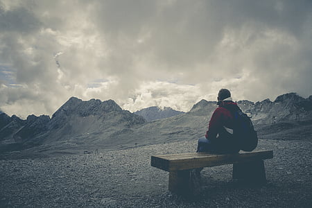 person carrying backpack sitting on bench overlooking mountain ranges