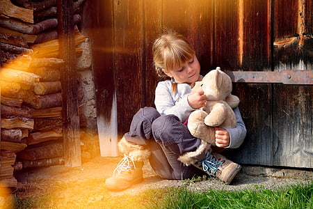 girl in grey sweater and black pants playing with brown teddy bear