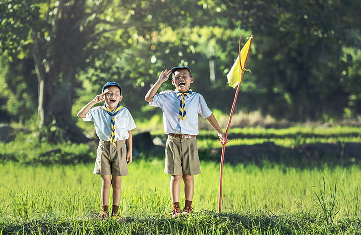 boy's scouts standing on green grass while holding flag