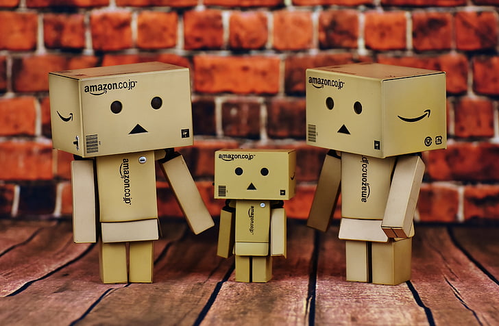 three brown Amazon cardboard human-designed boxes standing on brown surface near brick wall