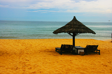 two lounge chairs under black wicker umbrella facing sea at daytime