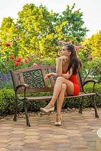 woman wears red mini dress sits on brown bench