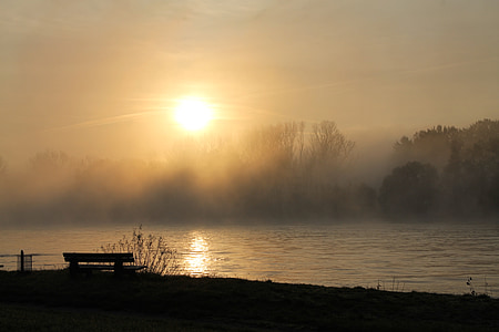 silhouette of bench near calm body of lake during sunset