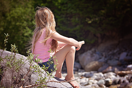 girl wearing pink top and blue shorts sitting on gray rock