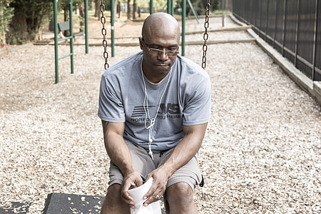 man wearing grey shirt sits on swing at park during daytime