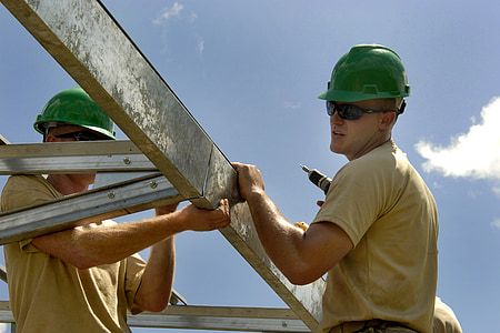 man wearing beige shirt and green safety helmet holding white steel bars