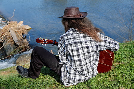 man playing guitar near body of water during daytime