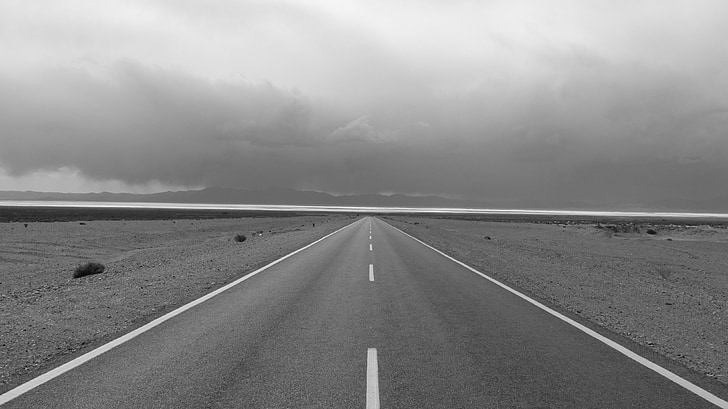 greyscale photo of road and sky with clouds
