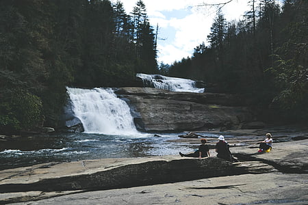 three people beside water falls during day time