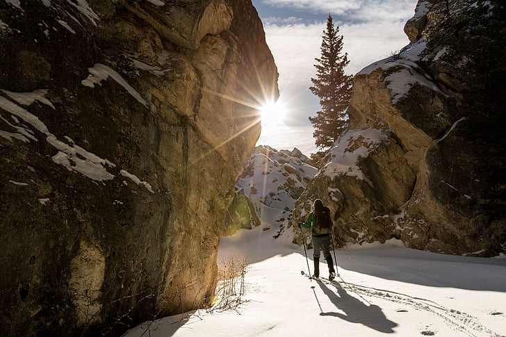 person walking on snow covered path surrounded by huge rocks overlooking sunrise
